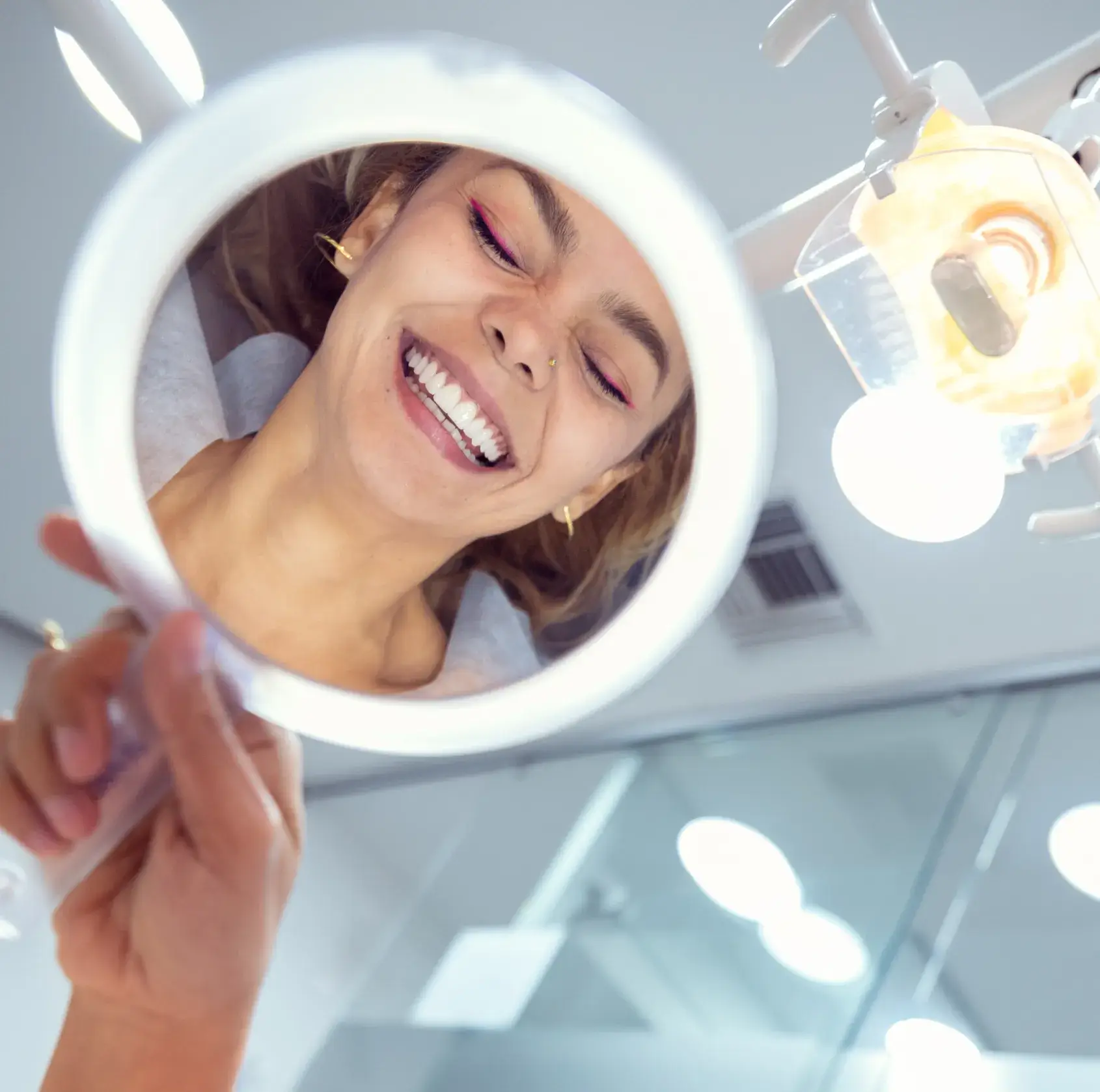 Woman smiling with straight teeth viewed through a dental mirror in a dentist's office.